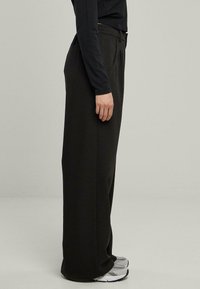 Crne, široke hlače s glatkom teksturom, s prednjim nabranim detaljima i elastičnom waistband-om, uparenim sa sivim tenisicama.