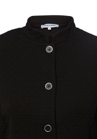 Zwarte textuurjacket met een mandarincol, voorzien van drie zilverkleurige knopen en een label met de tekst "MORE & MORE" aan de binnenkant van de hals.