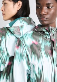 Lightweight hooded jackets featuring a blend of green, black, and pink abstract patterns; smooth texture with snap closures and drawstrings.