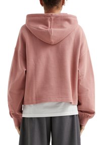 Roze cropped hoodie van textuurstof, met een trekkoordcapuchon en losse mouwen, gelaagd over een wit shirt.