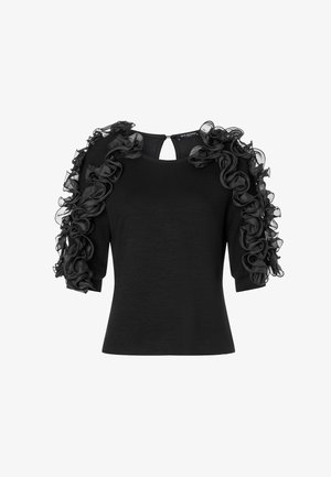 Zwart topje met korte mouwen, voorzien van gerimpelde zwarte organza accenten langs de schouders. Ronde halslijn en een detail met sleutelgat aan de achterkant.