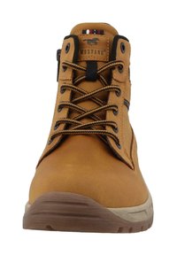 Botín de cuero marrón claro con cordones y costuras negras, suela de goma y un collar acolchado. Presenta una etiqueta de logo en la lengüeta y una franja en el costado.