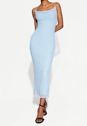 Kvinde iført en lyseblå midikjole i blonder med spaghettistropper, stylet med sorte, snørestøvler med høje hæle.