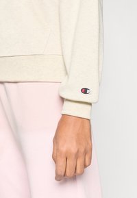 Μπεζ φούτερ με ριμπ μανσέτες, που διαθέτει κεντημένη λογότυπο λεπτομέρεια στο μανίκι. Ομαλή υφή υφάσματος και άνετη εφαρμογή.