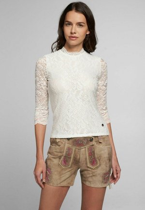 Weißes Spitzenoberteil mit drei Viertelärmeln, hohem Ausschnitt und taillierter Passform, kombiniert mit braunen Shorts mit Blumenstickerei und Seitentaschen.