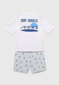 Biely krátky rukáv tričko s nápisom "SURF SUNSETS" a modrou grafikou s vlnami a slnkom. Svetlosivé šortky s námorníckym vzorom paliem.