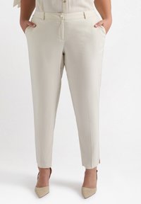 Kremowe, dopasowane spodnie o gładkiej fakturze, z przednimi kieszeniami i lekko zwężanym krojem. Wyposażone w zapięcie na guziki i zamek błyskawiczny.