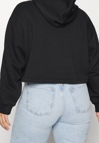 Svart beskuren huvtröja med dragsnodd vid huvan, med långa ärmar och en avslappnad passform, i kombination med ljusblå jeans med hög midja.