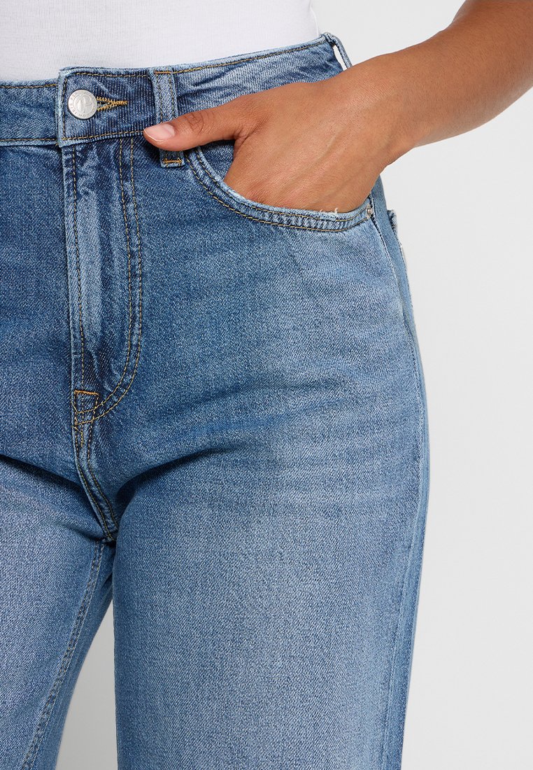 Jasnoniebieskie dżinsy z wysokim stanem o gładkiej teksturze, z kieszeniami z przodu, metalowym guzikiem i kontrastowym przeszyciem.