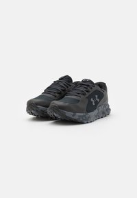 Chaussures de sport noires avec un dessus texturé, des lacets plats et une semelle à motif camouflage. Conçues pour l'adhérence et le soutien.