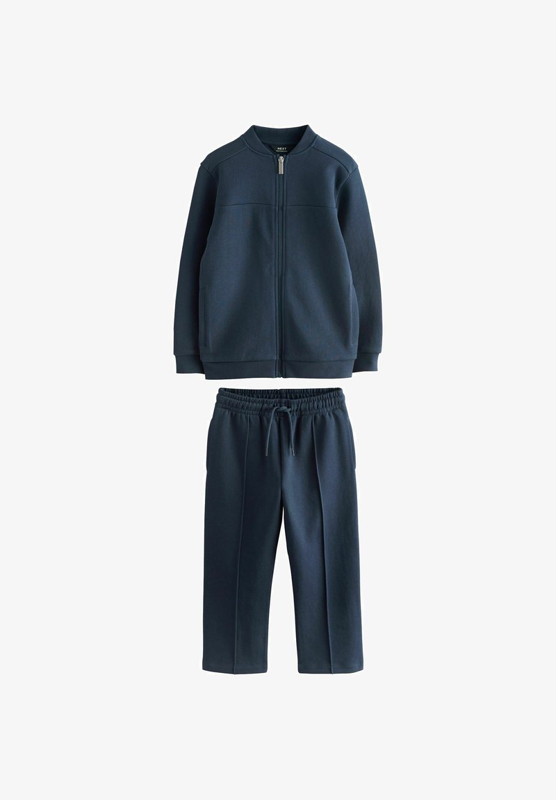Granatowa bluza z zamkiem błyskawicznym, z prążkowanym kołnierzem oraz dopasowanymi spodniami dresowymi z elastycznym ściągaczem w pasie.