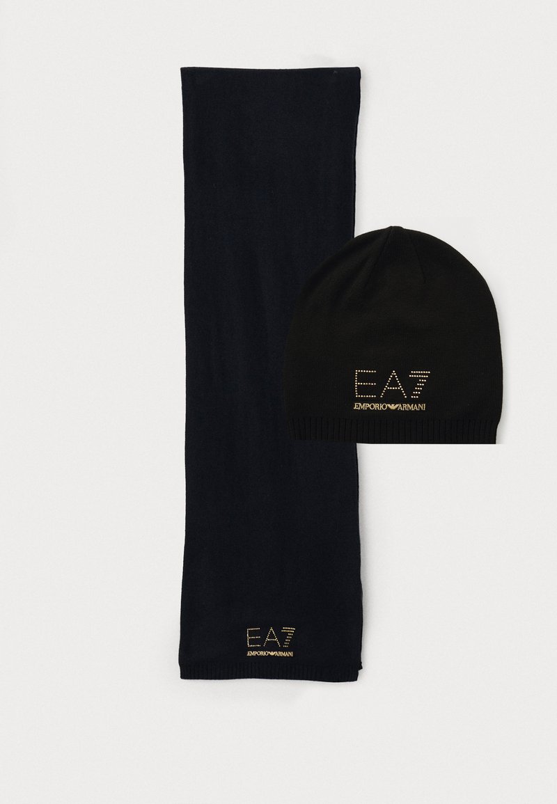 Zwarte gebreide beanie en lange sjaal, beide gemaakt van zachte stof. De sjaal is effen; de beanie heeft een metallic logo "EA7 EMPORIO ARMANI" in goud.