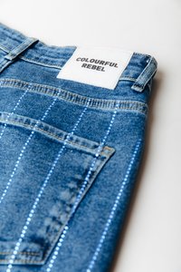 Jeans de denim en azul con una distintiva etiqueta blanca que dice "COLOURFUL REBEL". Presentan costuras azules a rayas y un diseño clásico de bolsillo trasero.