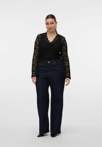 Haut noir en dentelle à manches longues avec un col en dentelle, associé à un jean en denim bleu foncé taille haute et des escarpins noirs à bout pointu.