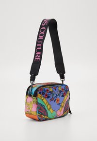 Barevná vzorovaná kabelka obdélníkového tvaru, s zipovým uzávěrem a černým popruhem s nápisem "COUTURE" v růžové barvě. Materiál je texturovaná tkanina.