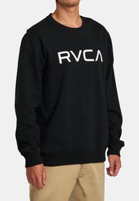 Sweatshirt noir à col rond en coton avec le logo "RVCA" blanc sur le devant. Comprend des poignets et un ourlet côtelés pour un ajustement confortable.