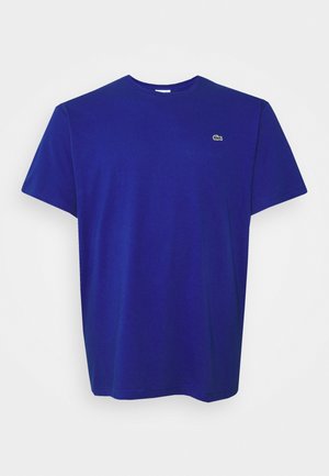 Blauwe katoenen t-shirt met een ronde hals, korte mouwen en een klein groen geborduurd logo op de linkerborst. Gladde textuur.