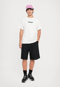 Hvit kortermet t-skjorte med svart logo, svarte shorts, svarte joggesko og en rosa caps. Enkel, avslappet urbane mote design.