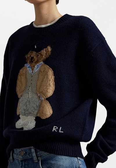 Marineblauwe gebreide trui met een geborduurde beer in een ontwerp met jas en hoed, met witte "R.L"-letters aan de zoom en geribde manchetten.