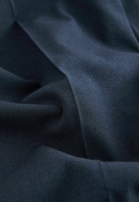 Jūras zilas krāsas audums ar gludu tekstūru, izkārtots ar krokām. Materiāls izskatās viegls un nedaudz atstarojošs, demonstrējot smalku spīdumu.