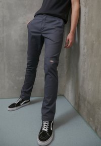 Szare spodnie dresowe z bocznymi kieszeniami i wzmocnieniami na kolanach, zestawione z czarno-białymi sneakersami o niskim profilu.