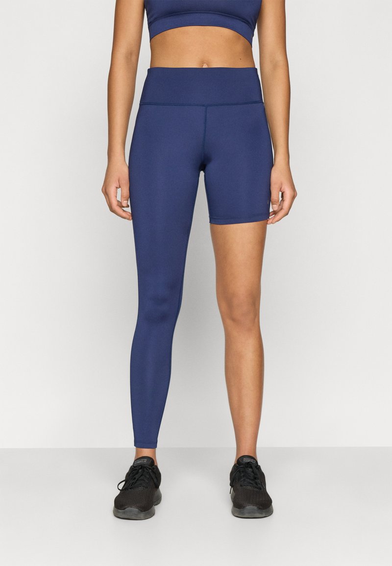 Tmavomodré športové legíny s vysokým pásom, s asymetrickým dizajnom so jednom celou nohavicou a druhou dĺžky do polovice stehna.