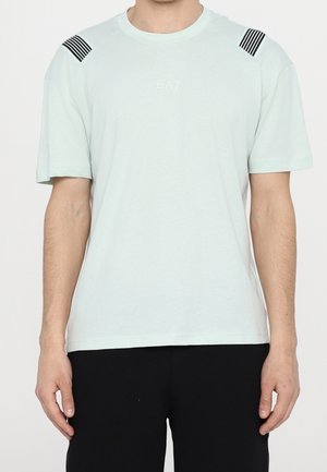 T-shirt vert menthe clair à manches courtes, avec des accents rayés noirs sur les épaules et un petit logo EA7 sur la poitrine. Texture douce.