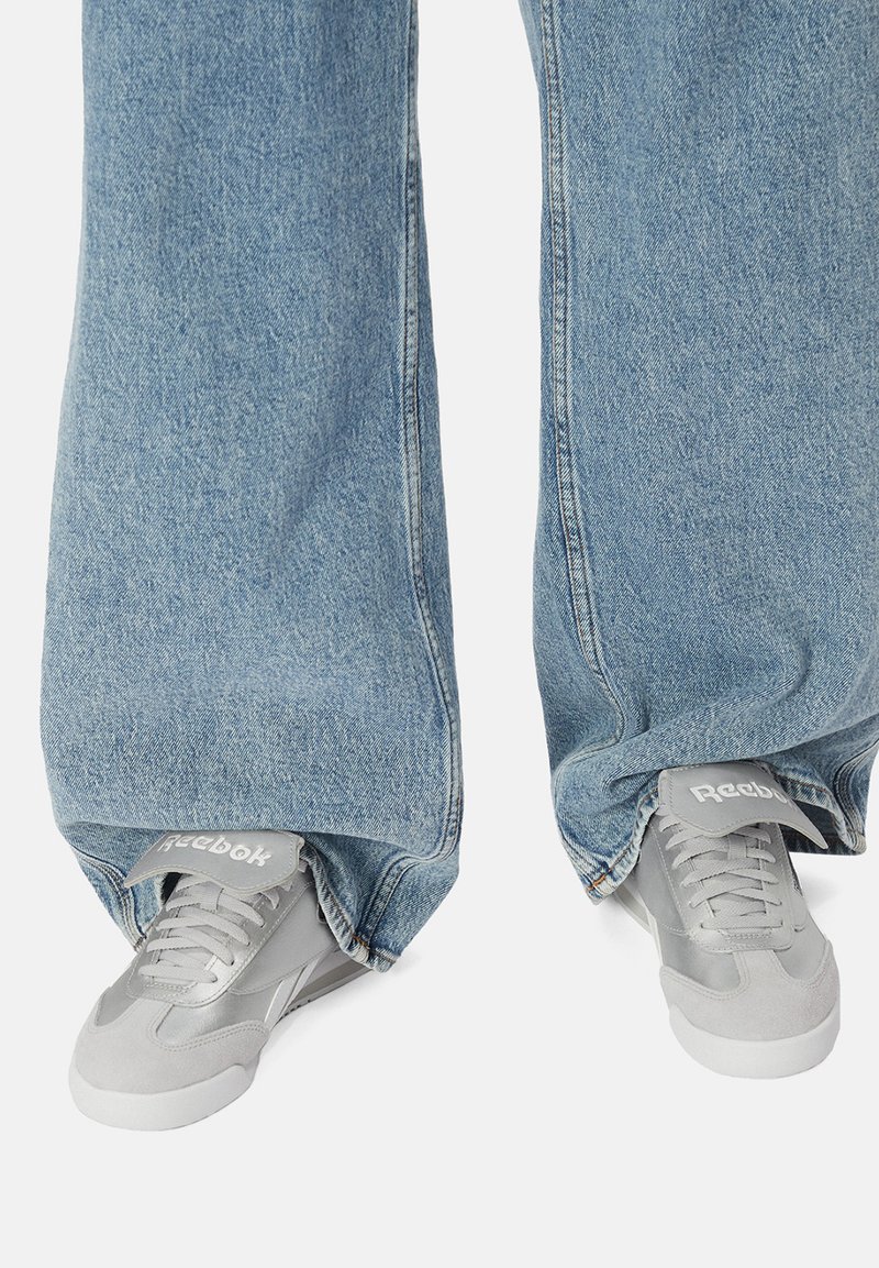 Pantaloni a gamba larga in denim azzurro chiaro abbinati a sneakers Reebok grigie con accenti in suede grigio e logo sulla linguetta.
