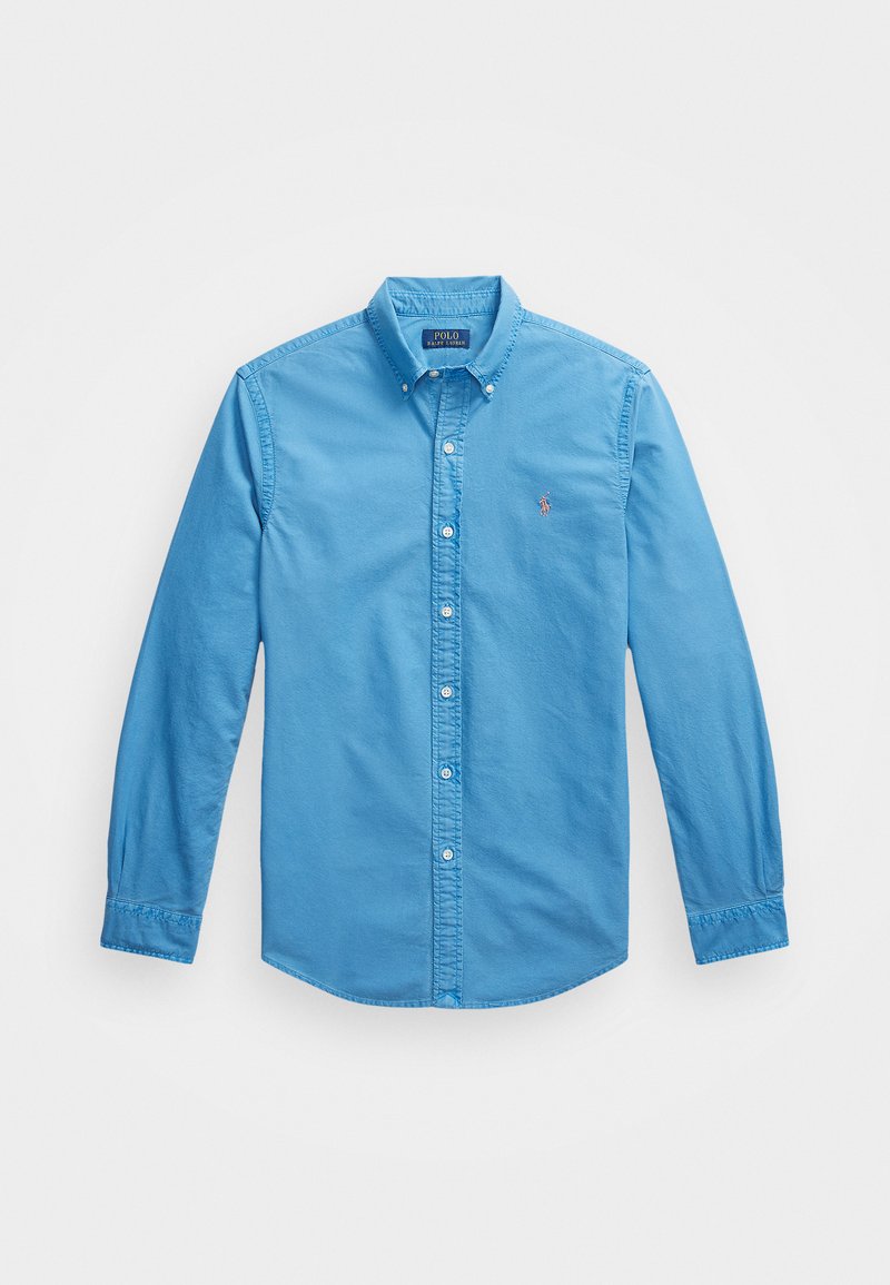Šviesiai mėlynas medvilninis marškinis su ilgomis rankovėmis, mygtukų uždarymu, priekine apykakle ir mažuoju išsiuvinėtu logotipu kairėje krūtinės pusėje.