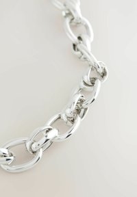 Cadena de metal plateado con grandes eslabones entrelazados. Textura suave con un acabado brillante. Cada eslabón presenta una forma ovalada redondeada.
