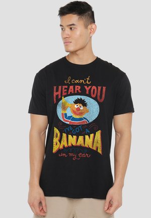 Black cotton t-shirt featuring a colorful graphic with text: "I can't HEAR YOU, I've got a BANANA in my ear," paired with a cartoon character holding a banana.