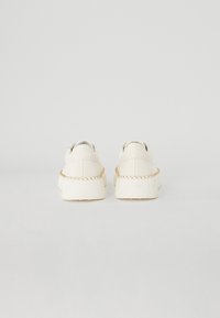 Witte sneakers met een gestructureerde afwerking, voorzien van een dikke zool en een gevlochten accent rond de hiel. Eenvoudig en minimalistisch ontwerp.