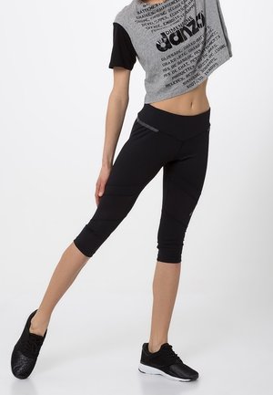 Czarne legginsy typu capri o gładkiej fakturze i subtelnym wzorze. Połączone z krótkim szarym T-shirtem z nadrukiem i czarnymi sportowymi butami.