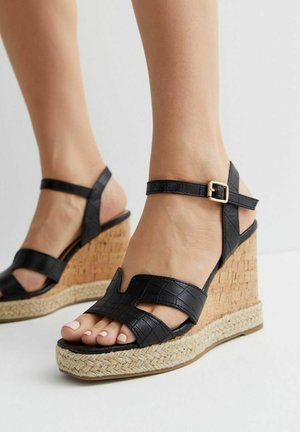 Sandalias de cuña de cuero de cocodrilo sintético negro con suela de yute trenzada, que cuentan con dos correas anchas y un hebilla en el tobillo ajustable.