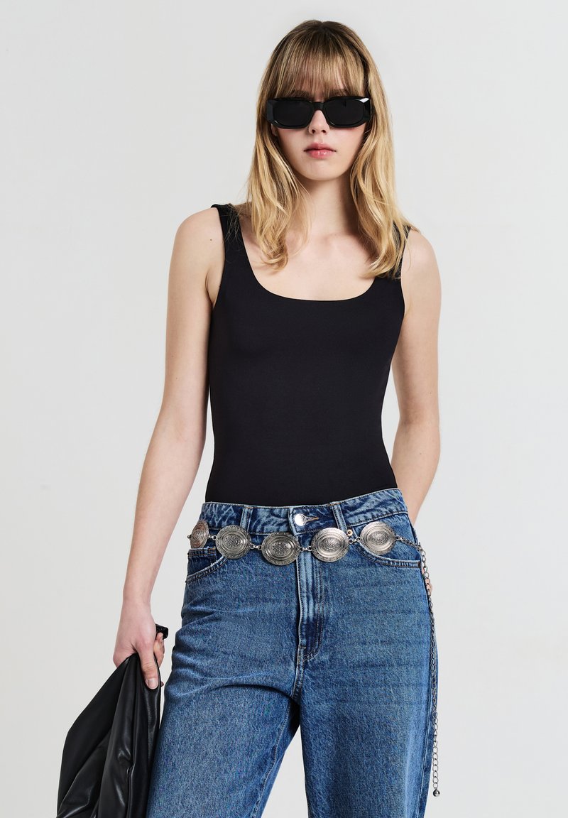 Body senza maniche nero, design a vita alta; abbinato a jeans di denim blu a vita alta con una cintura argentata con accentuazione circolare.