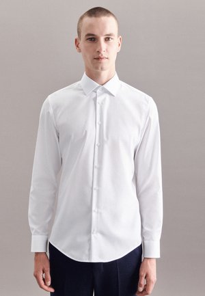 Witte langjarige button-up shirt met een puntige kraag, gladde stof en gebogen zoom, gedragen met donkere broek.