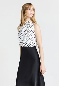 Blusa a pois bianca e nera con scollatura drappeggiata. La modella indossa una gonna nera in satin, che mette in risalto linee eleganti.