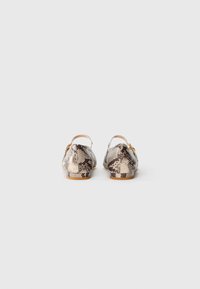 Un paio di scarpe slingback flat con motivo serpente beige e nero e piccola fibbia dorata, viste da dietro su uno sfondo bianco.