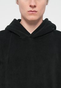 Zwarte fleece hoodie met een zachte textuur, voorzien van een V-vormige halslijn en een trekkoordcapuchon. Geen zichtbare logo's of patronen.
