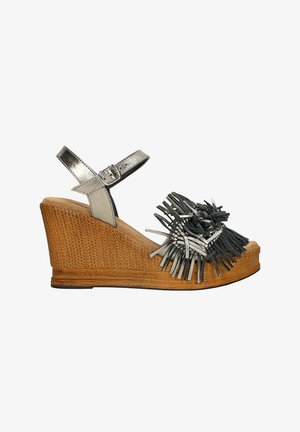 Sandalia de cuña con suela de yute trenzado, correa metálica plateada en el tobillo y adornos de flecos en negro y plata en la punta.