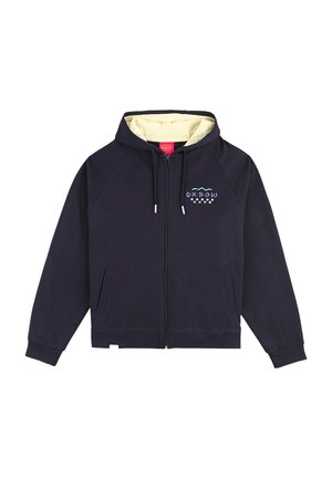 Haut de sweatshirt zippé bleu marine avec une doublure intérieure crème, présentant un petit logo coloré sur la poitrine et deux poches latérales. Matériau en coton.