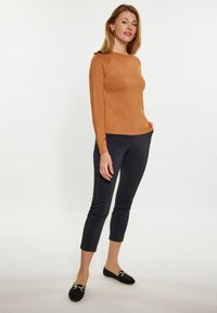 Bruine, slim-fit trui met lange mouwen, gecombineerd met marineblauwe cropped broek en zwarte loafers met gouden hardwareaccenten. Eenvoudige, gladde texturen.