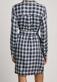Abito camicia a quadri blu navy e bianco con maniche lunghe, colletto, vita cintrata e bottoni. Il retro presenta un yoke e un dettaglio a pieghe.