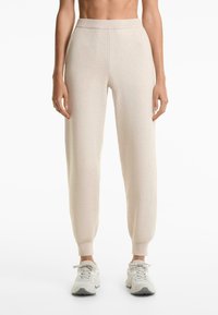 Light beige jogger pants with a ribbed waistband and cuffs, featuring a soft texture and relaxed fit, paired with light gray sneakers.