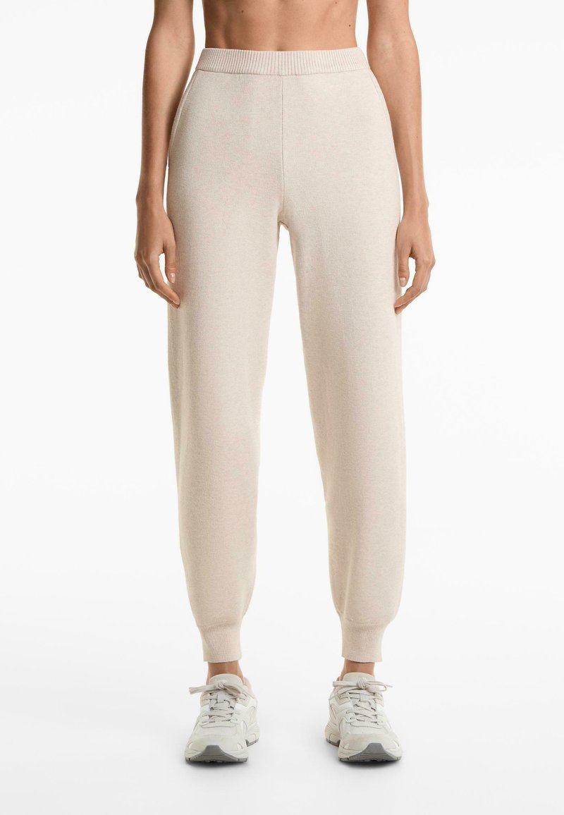 Light beige jogger pants with a ribbed waistband and cuffs, featuring a soft texture and relaxed fit, paired with light gray sneakers.