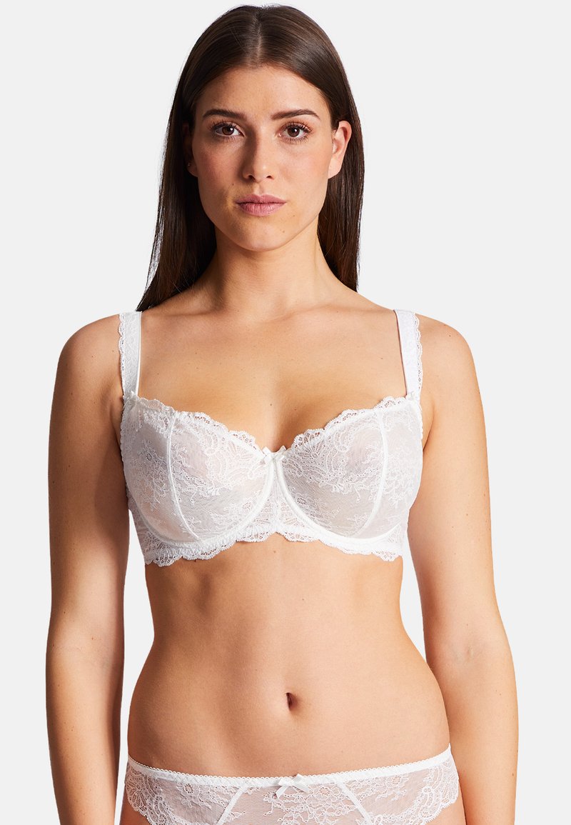 Soutien-gorge en dentelle blanche avec un motif floral, avec armatures de soutien et bretelles réglables. Bords festonnés notables et un petit nœud au centre.