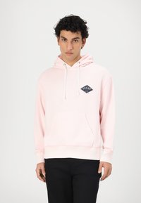 Helle rosa Kapuzenpullover aus Baumwollmischung, mit einer Fronttasche und verstellbarem Kordelzug an der Kapuze. Marineblaues Logo-Patch auf der linken Brust. Lange Ärmel.