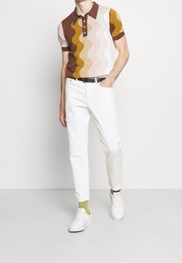 Pruhovaná polo triko v přírodních tónech, doplněné bílými džínami. Podtrženo černým opaskem a zelenými ponožkami. Dokončeno bílými teniskami.