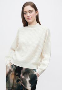 Kremfarvet strikket sweater med tekstureret mønster, ribbet halsudskæring og manchetter, kombineret med mørke bukser med blomsterprint.