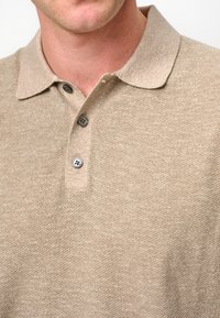 Beige textured polo shirt with a collar, featuring two buttons in contrasting colors, and a slightly flecked surface pattern.